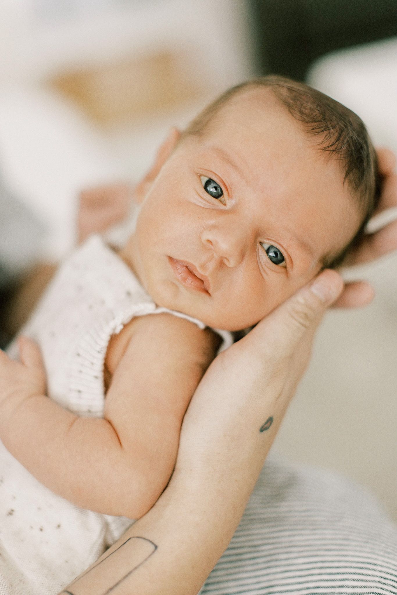 Close-up portraits of a baby in white clothing lying on striped bedding.