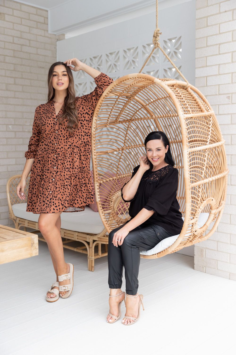 Models lounging in hanging rattan chair wearing leopard print dress and black outfit.