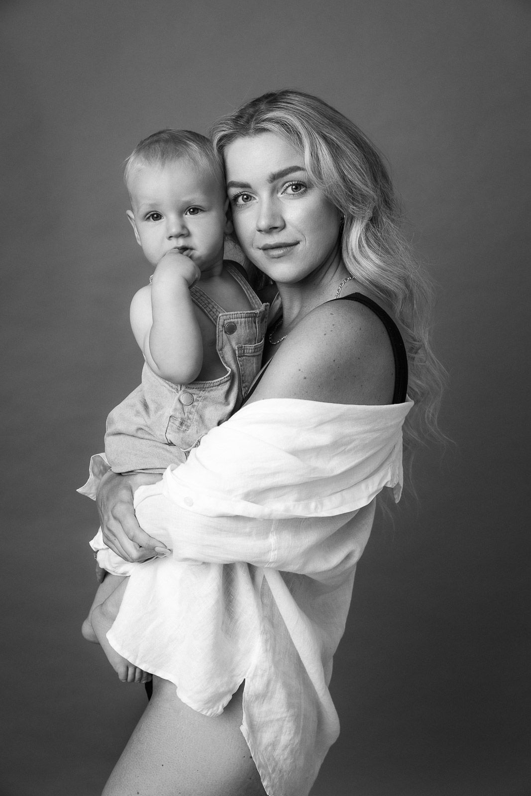 A black and white portrait series showing tender moments between a parent and baby in matching white clothing.