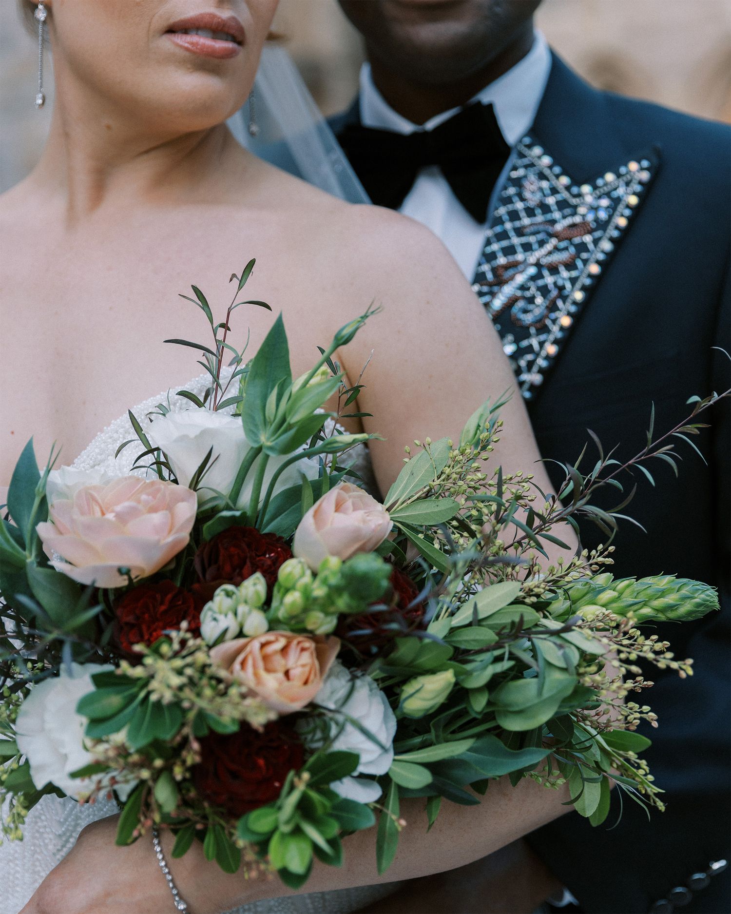 Close-up of a romantic wedding bouquet featuring pink roses, greenery, and burgundy blooms.
