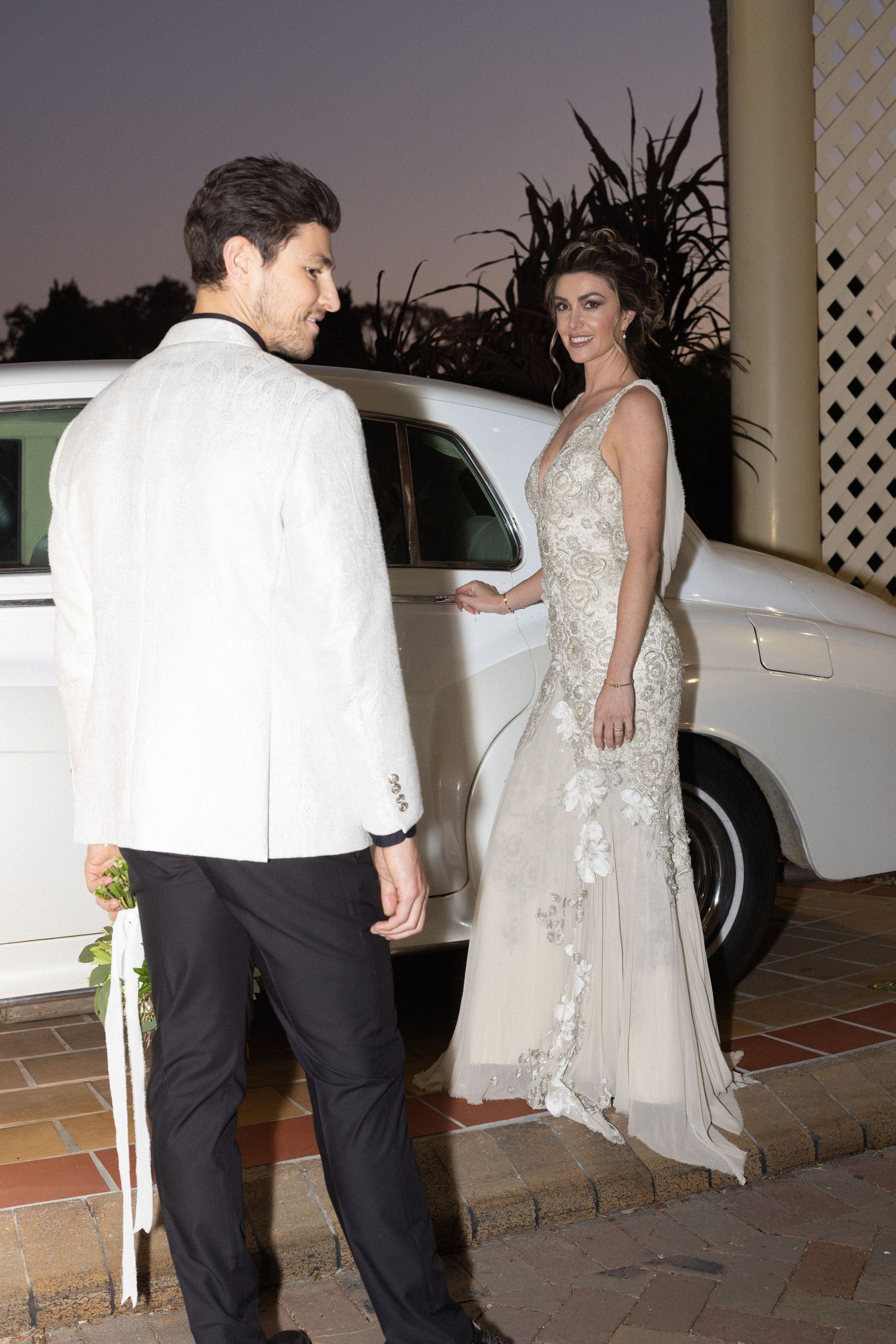 Wedding couple walking together at night outside a white building with columns and lattice details.