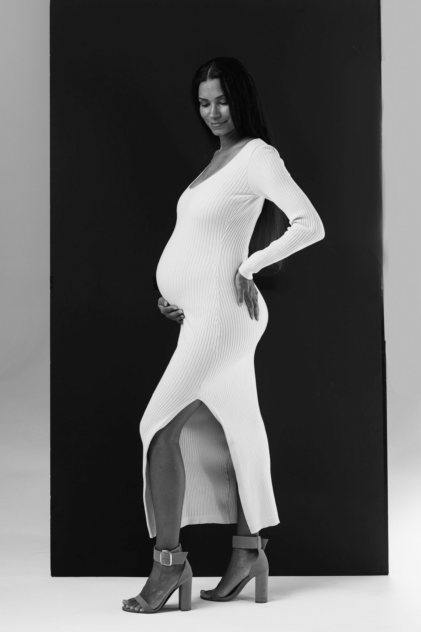 Fashion model in white ribbed sweater poses against black background in artistic black and white studio photography.
