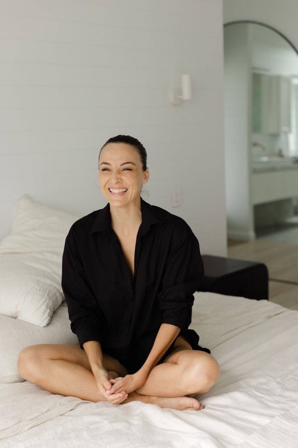 Lifestyle photography in black loungewear on white bedding in modern bedroom setting.