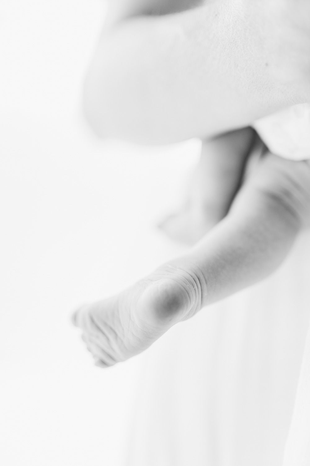 Artistic black and white close-up of baby's tiny foot against white background.
