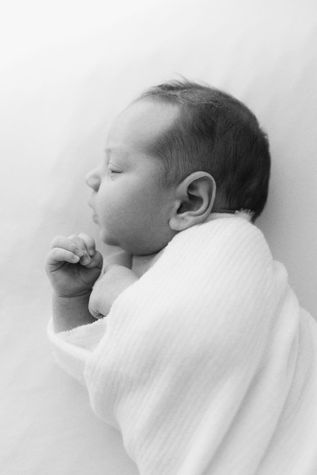 A black and white portrait showing a sleeping baby swaddled in white cloth by a Gold Coast Newborn Photographer