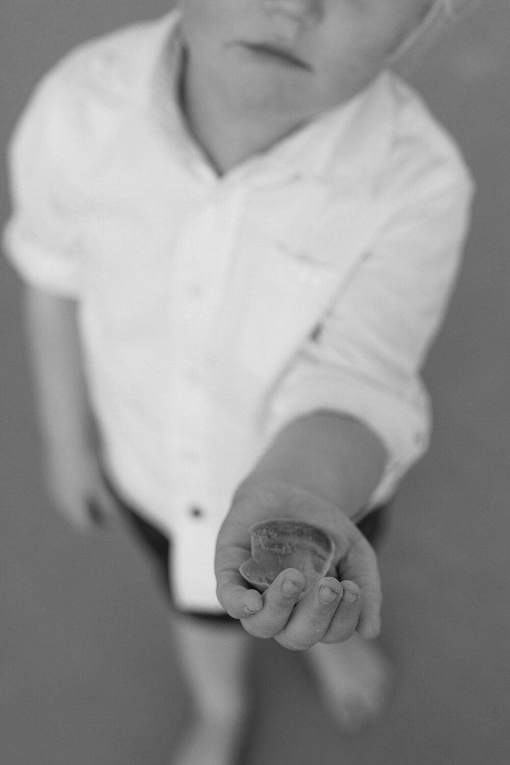 Black and white close-up of a young child in white shirt reaching out their hand toward the camera.
