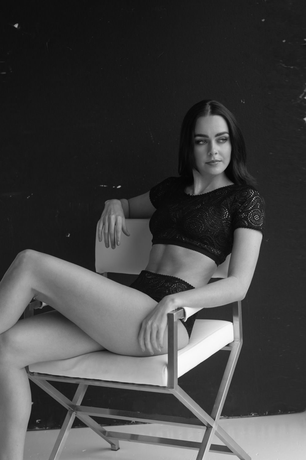 Dramatic black and white portrait of woman in crop top seated on director's chair.