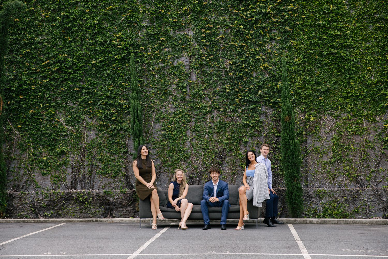 Wedding party members gathered casually against ivy-covered wall outdoors.