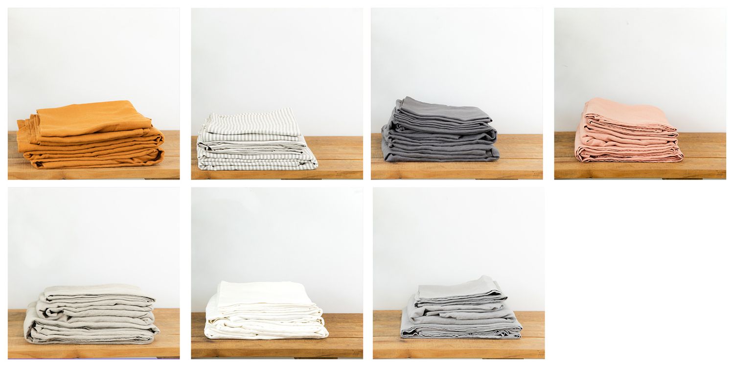 Collection of folded linens and textiles in earthy tones arranged on wooden surface.