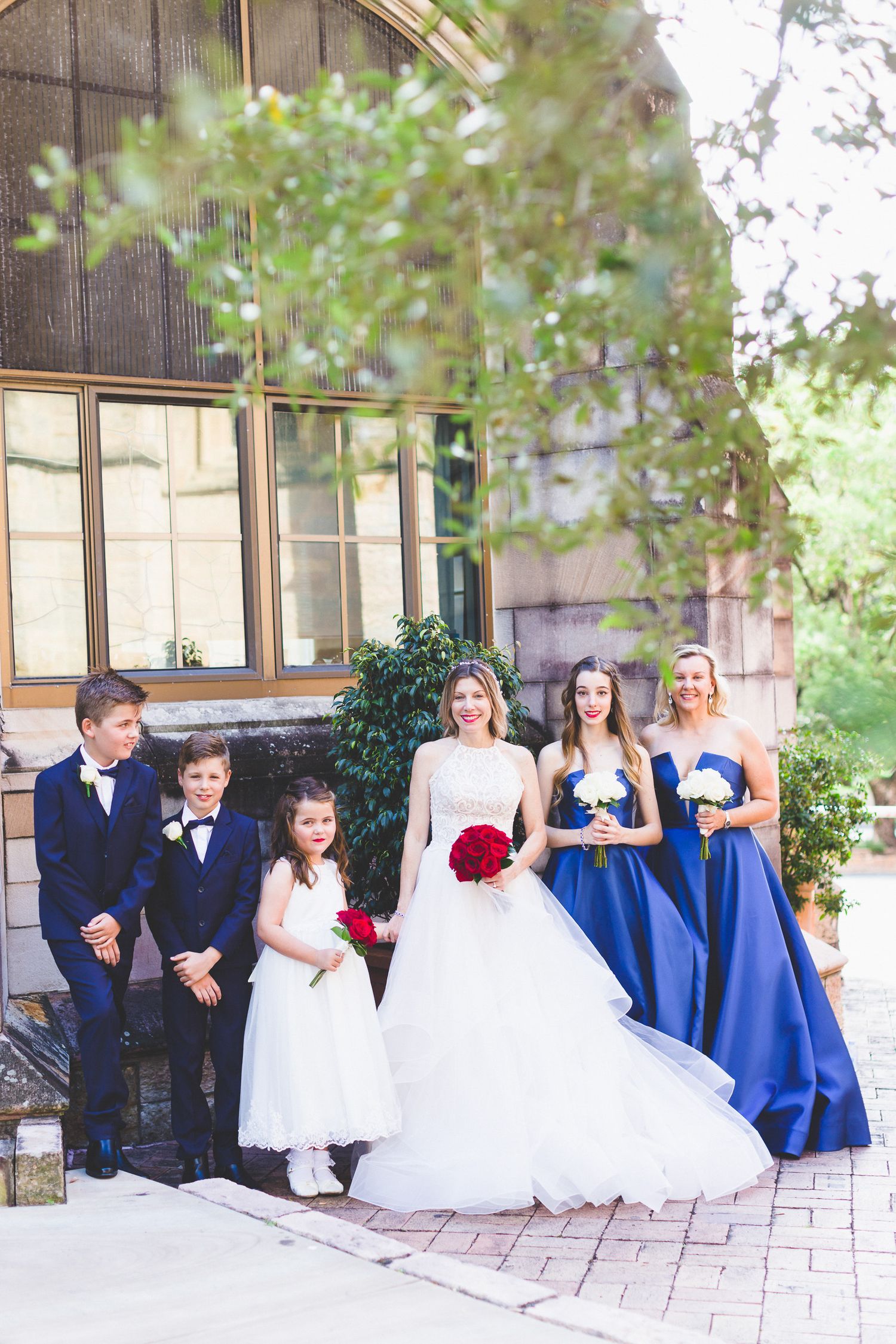 Wedding party in blue dresses and white gowns posed together on outdoor patio.