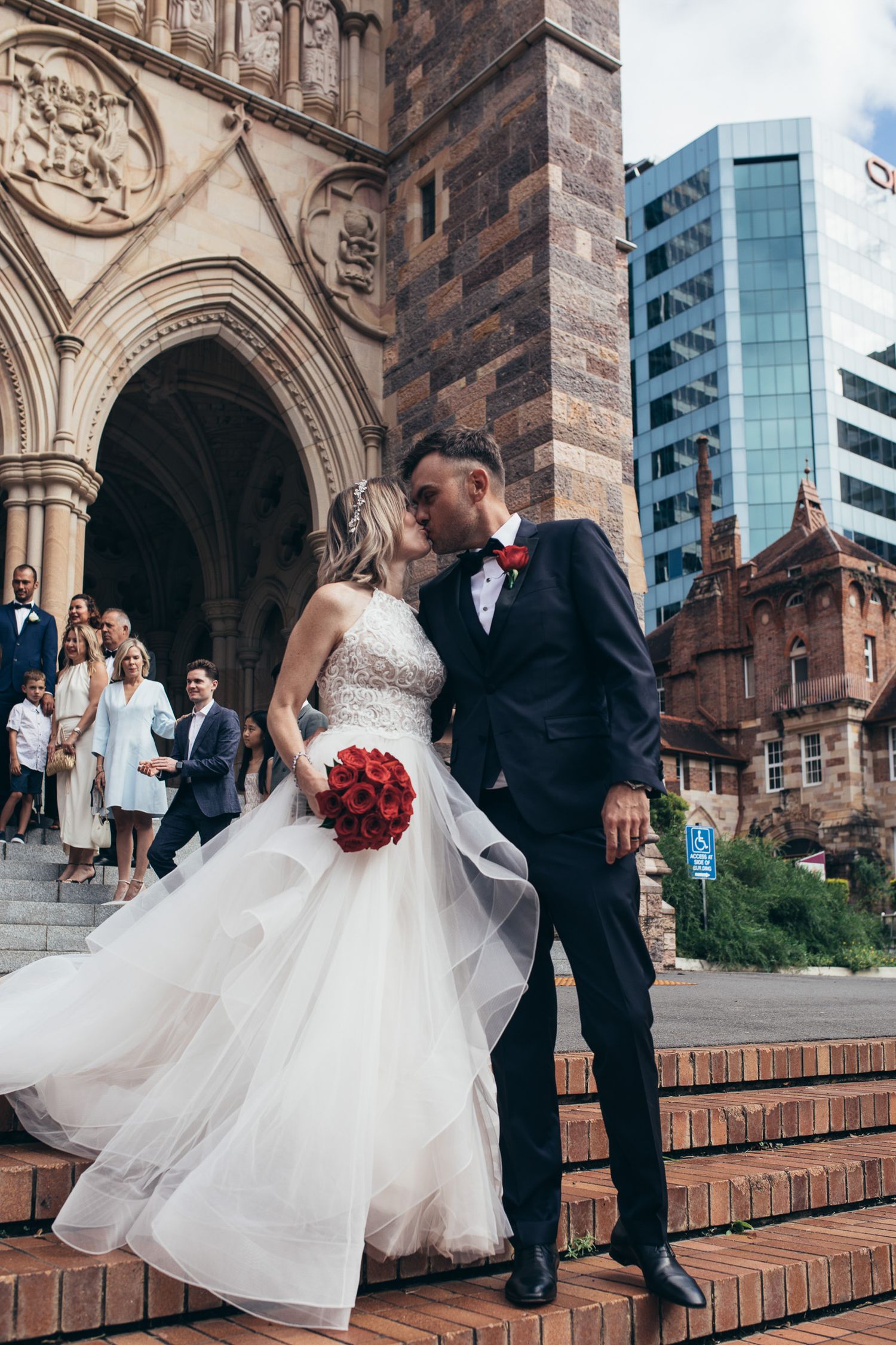 Wedding couple and party taking photos on brick steps of historic church building.