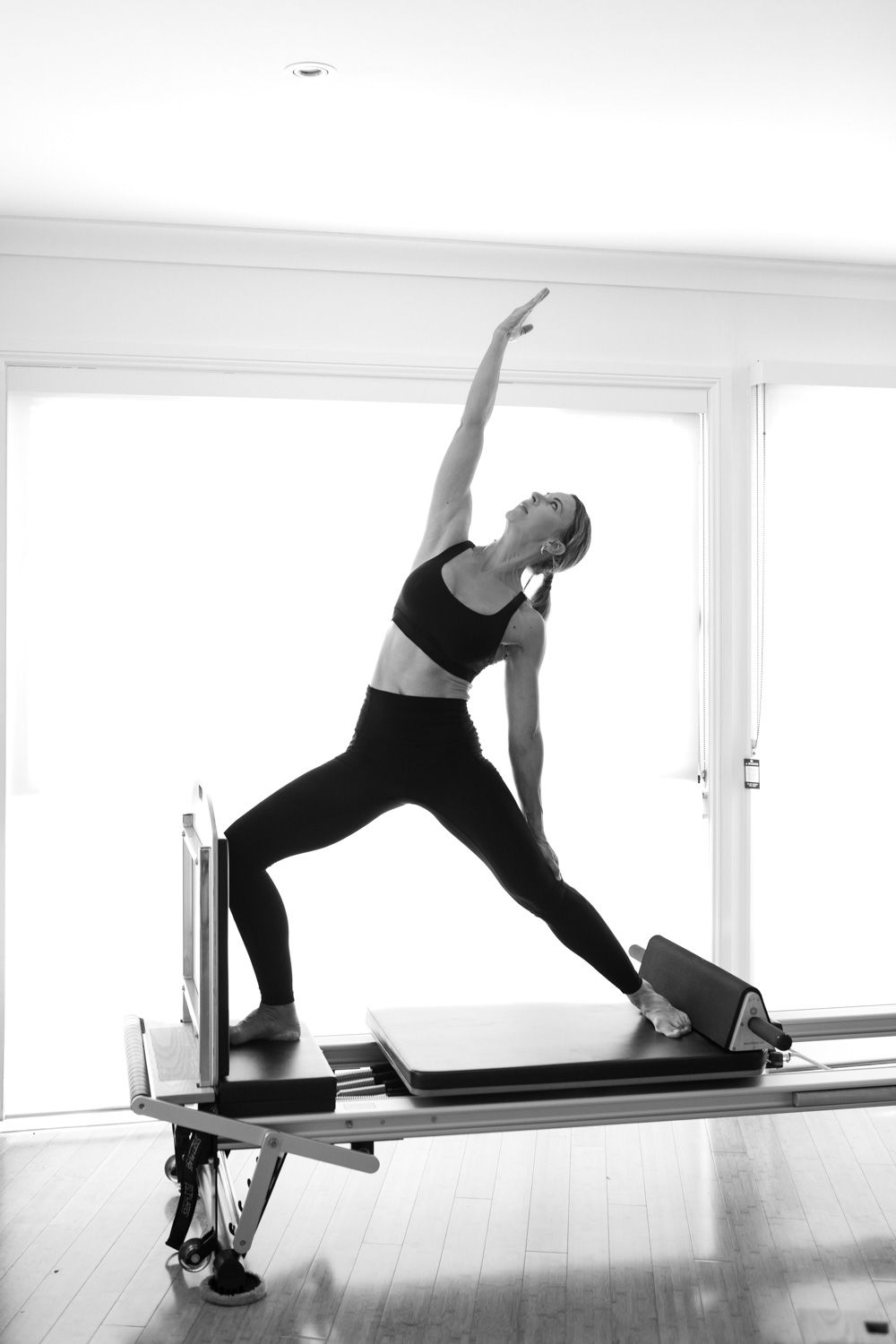 A person demonstrates a yoga sequence on a ballet barre in a bright white studio space.