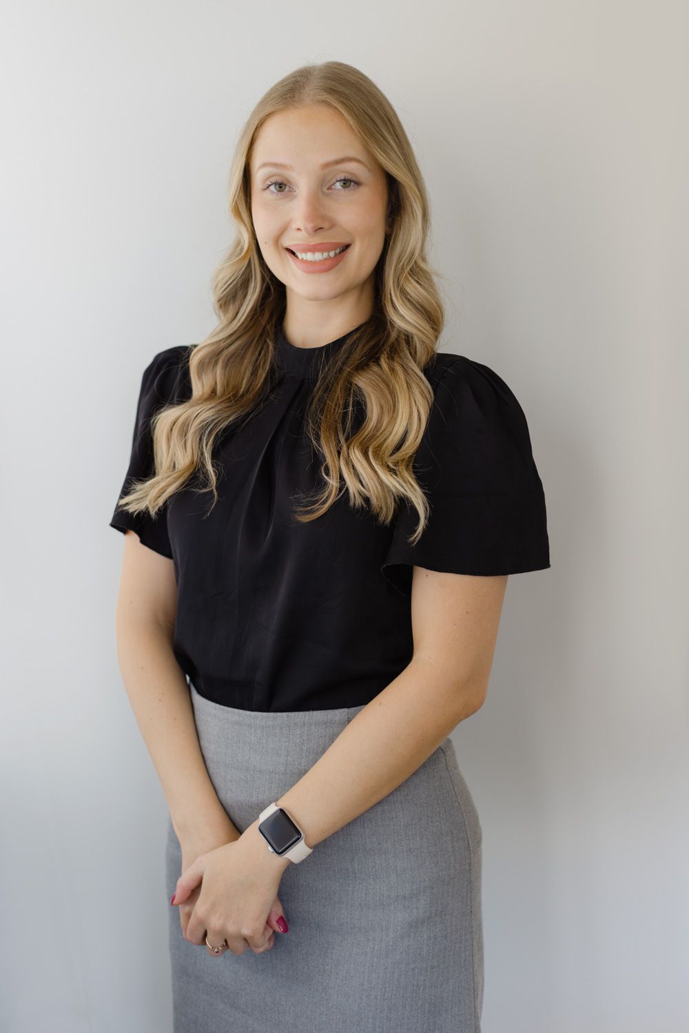 Professional portrait of someone wearing a black top and grey skirt against a white background.