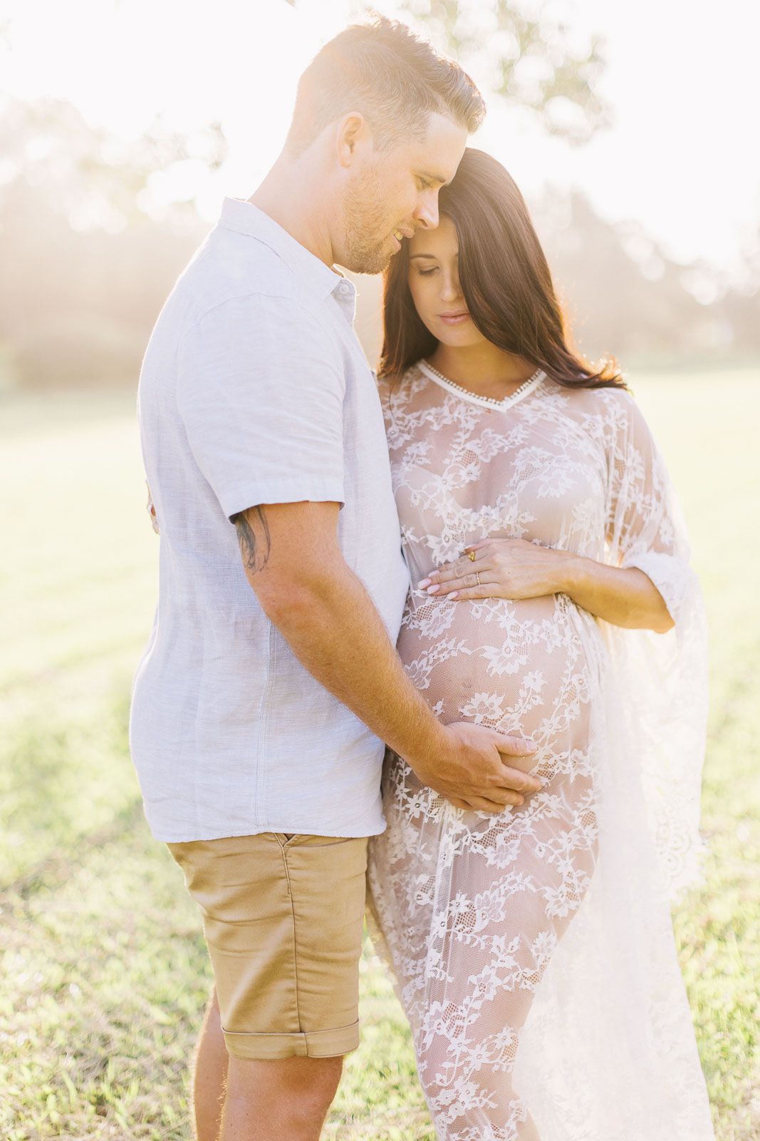Sun-drenched maternity photos in a field with couple in white and neutral tones.
