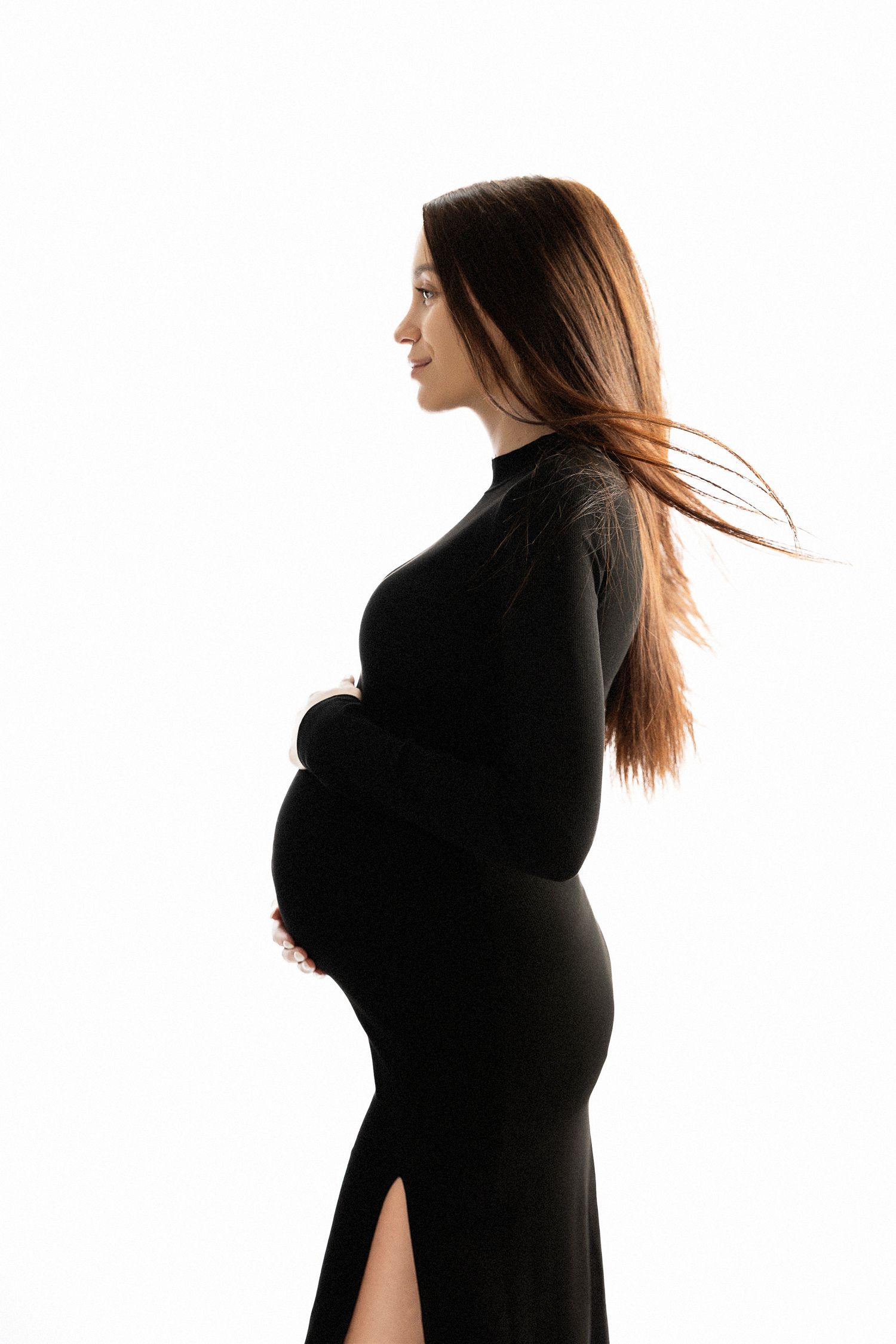 Silhouetted side profile maternity portrait in black dress against white background.