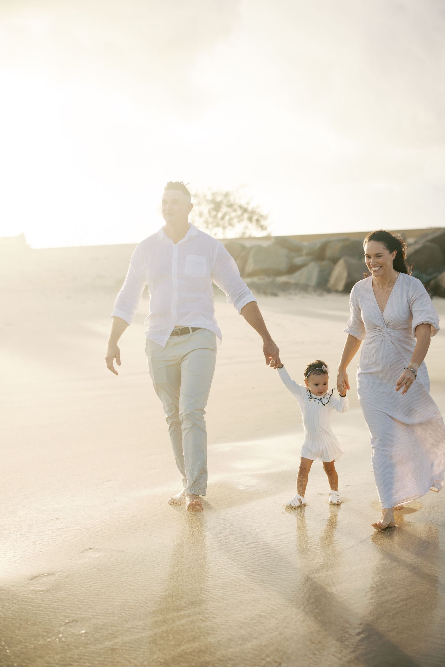 Sunlit beach scene with family walking together in white outfits during golden hour.