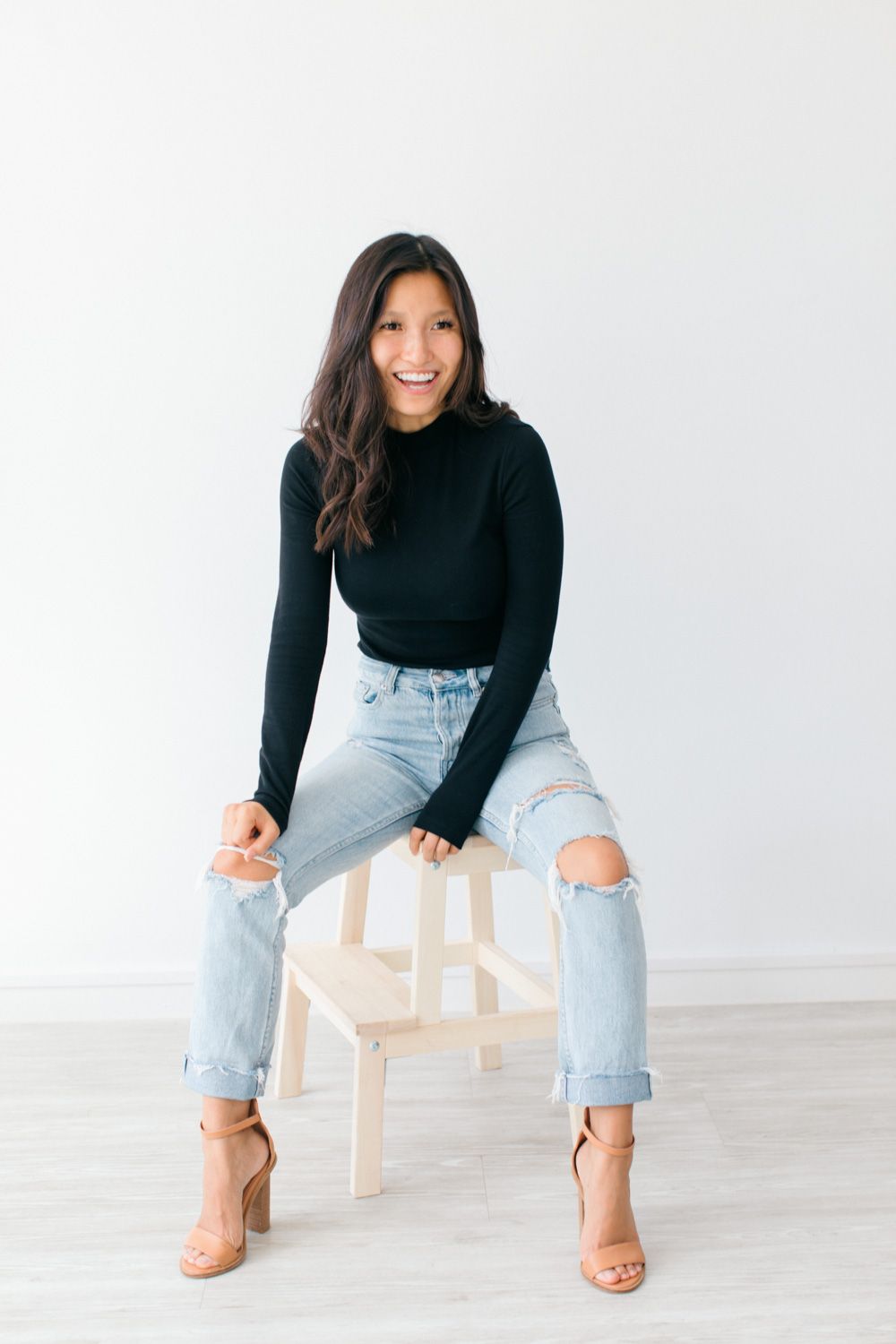 Casual lifestyle photos of woman in black turtleneck and ripped jeans sitting on white chair.
