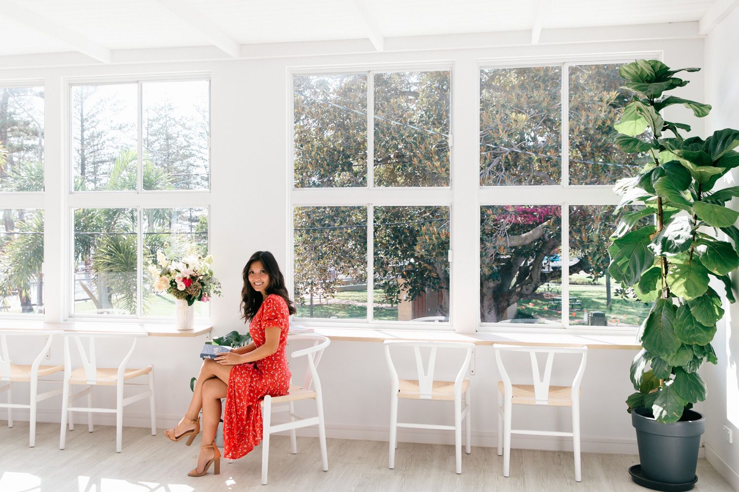 Bright and airy sunroom interior with white chairs arranged along glass windows overlooking a garden view.