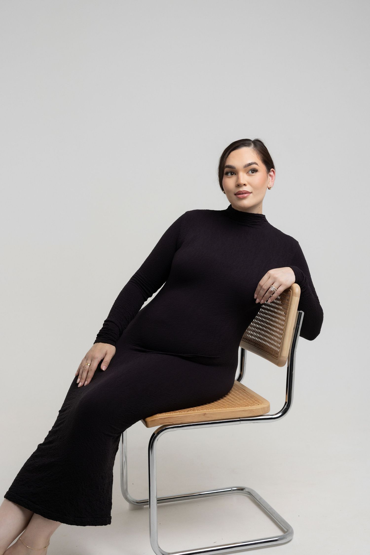 Stylish maternity portraits on modern wooden chair showing relaxed poses in black dress.