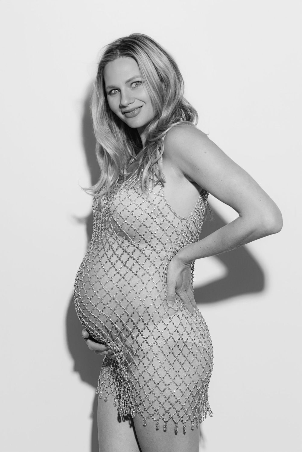 Black and white photo of a smiling pregnant woman in a beaded mini dress posing sideways.