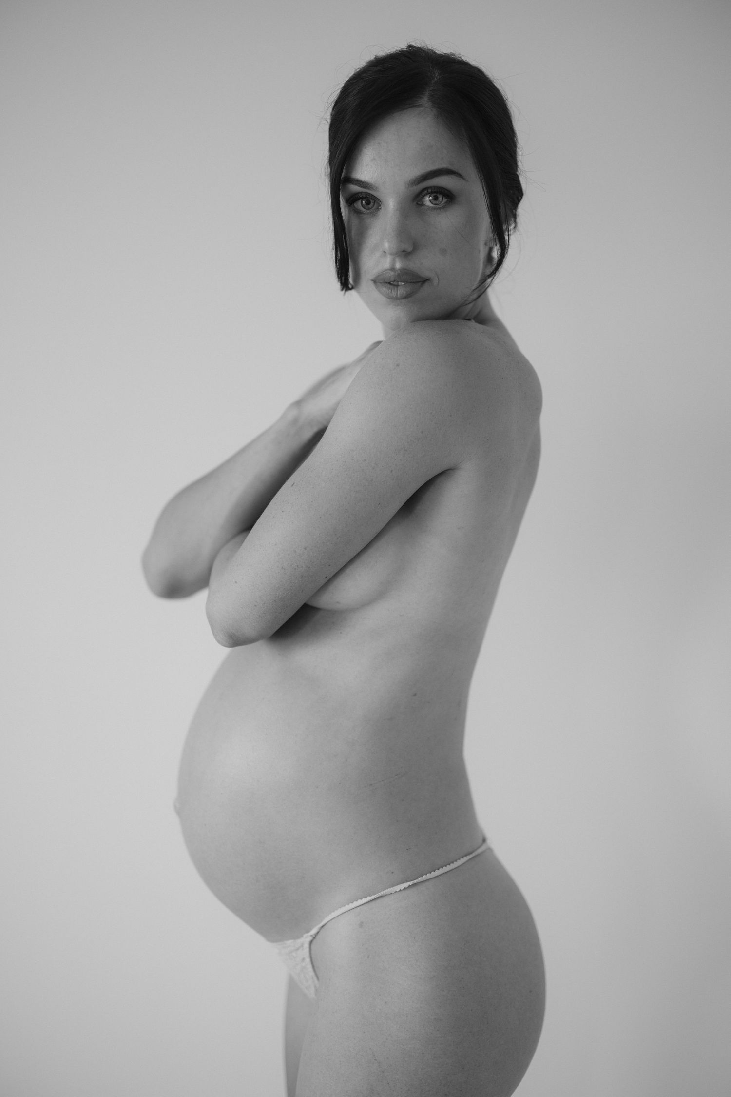 Black and white artistic maternity photo showing a side profile of an expectant mother in minimal clothing.