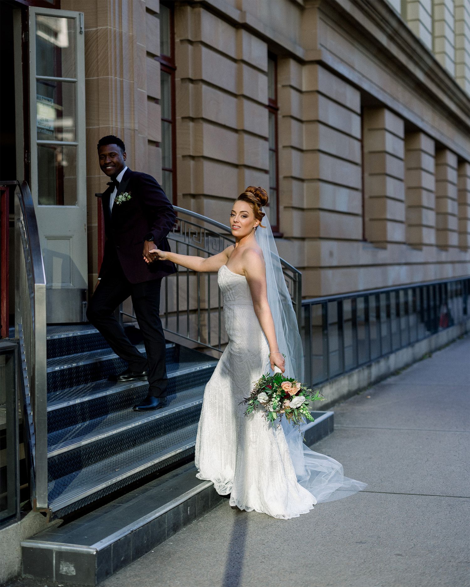 Wedding couple posing along a classic building exterior with columns and ramps.