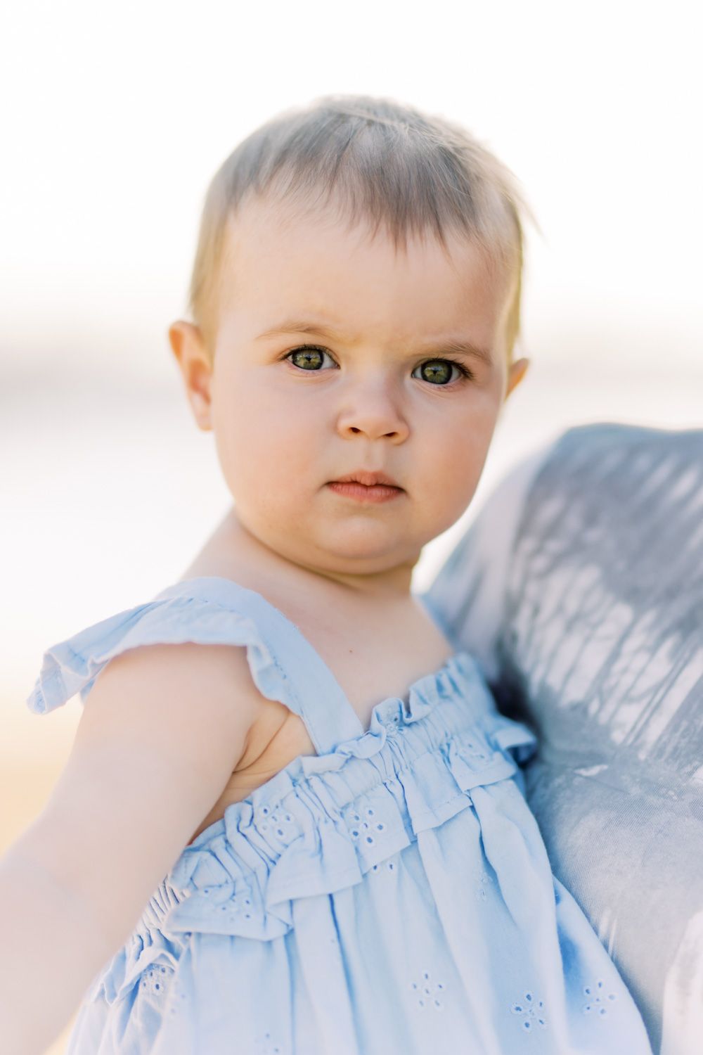 Baby wearing light blue ruffled dress in soft natural lighting.
