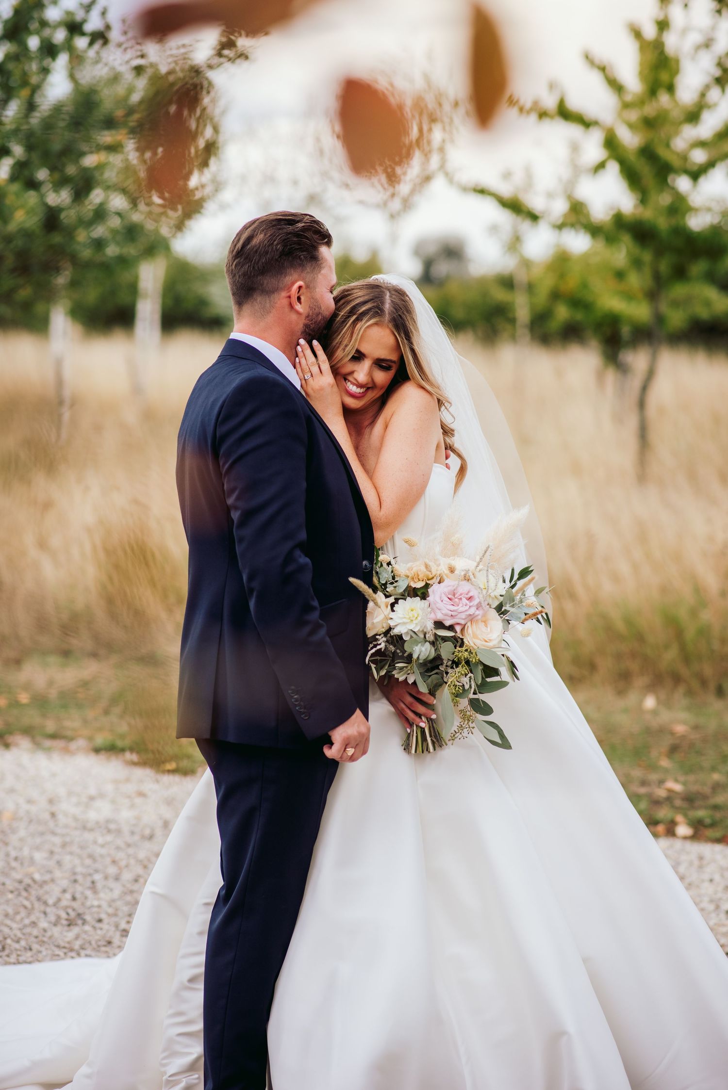 A romantic moment between newlyweds outdoors with a beautiful white wedding gown and bouquet of greenery.