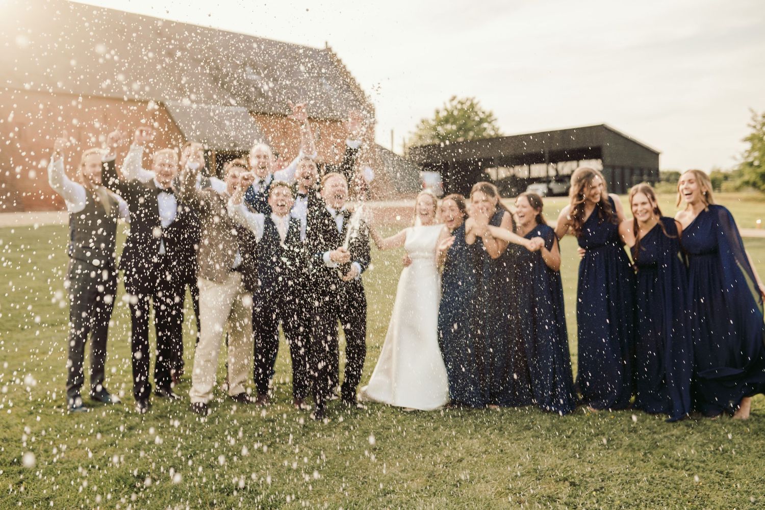Wedding party members celebrate with confetti in an outdoor setting at sunset.