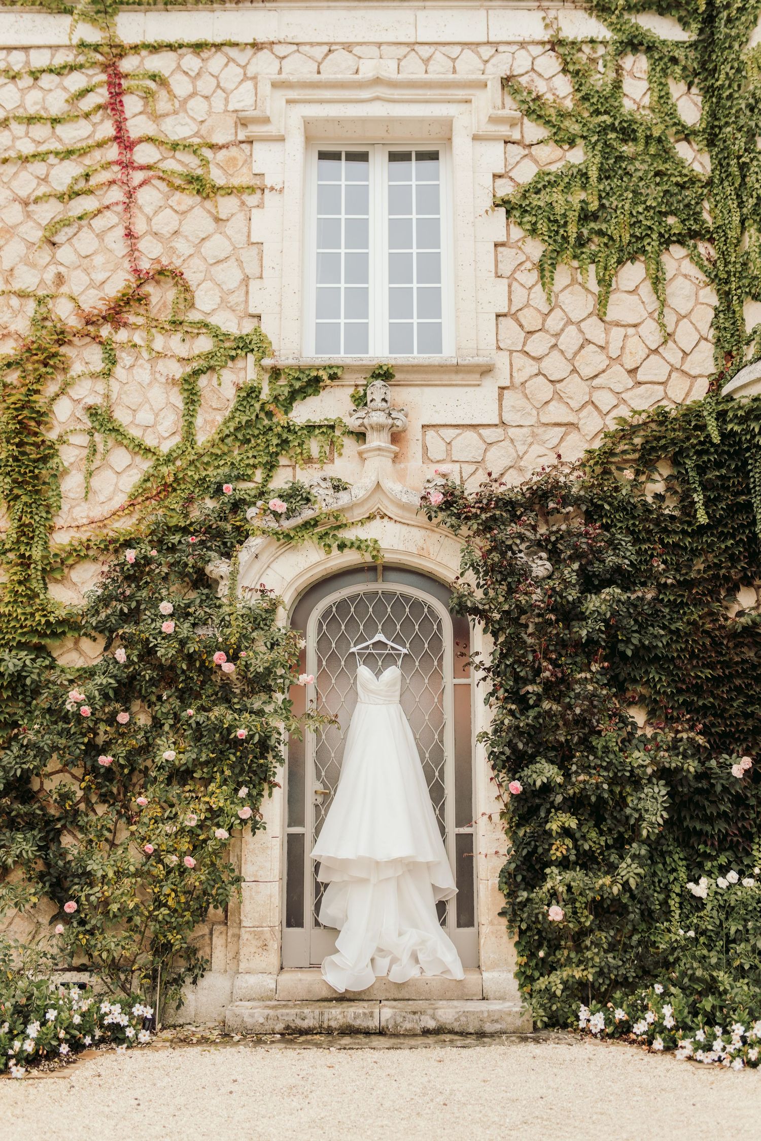 White wedding dress hanging outside stone villa with ivy covered walls.