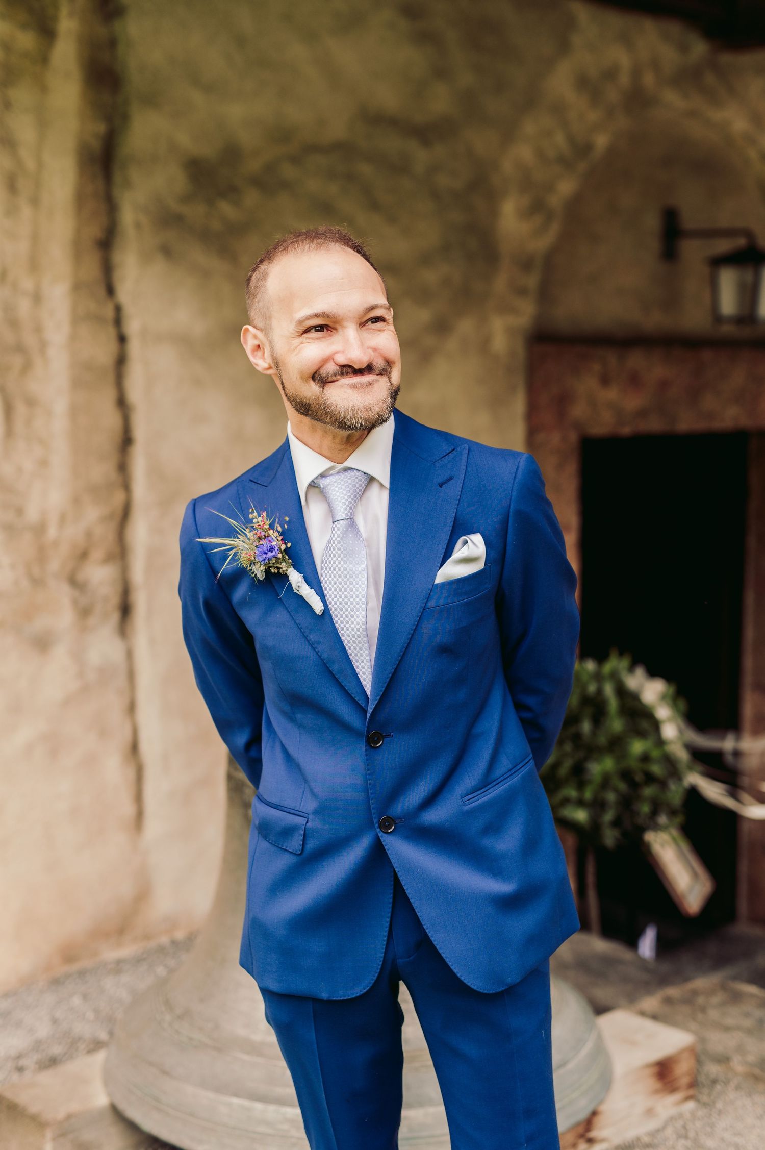 A groom in a bright blue suit and white tie smiles at his wedding while wearing a floral boutonniere. Spiez switzerland destination wedding