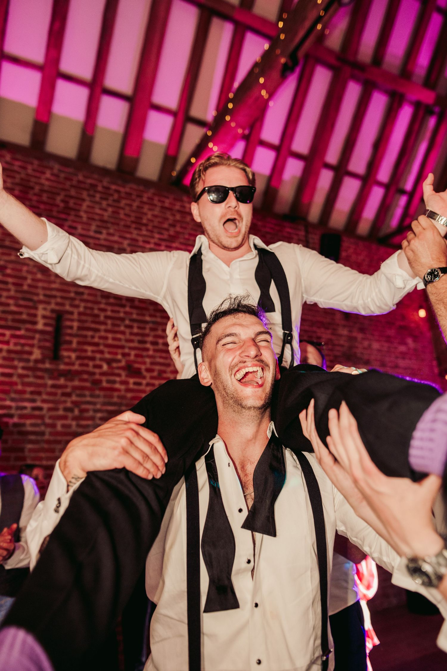 Partygoers celebrating energetically at a nightclub with brick walls and pink lighting in the background.