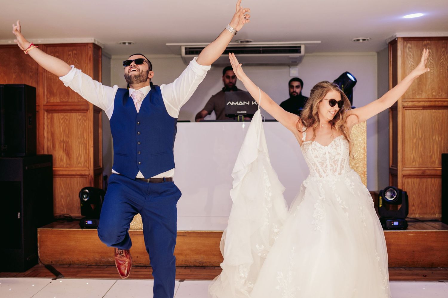 Joyful newlyweds dancing together at their wedding reception with arms raised in celebration.