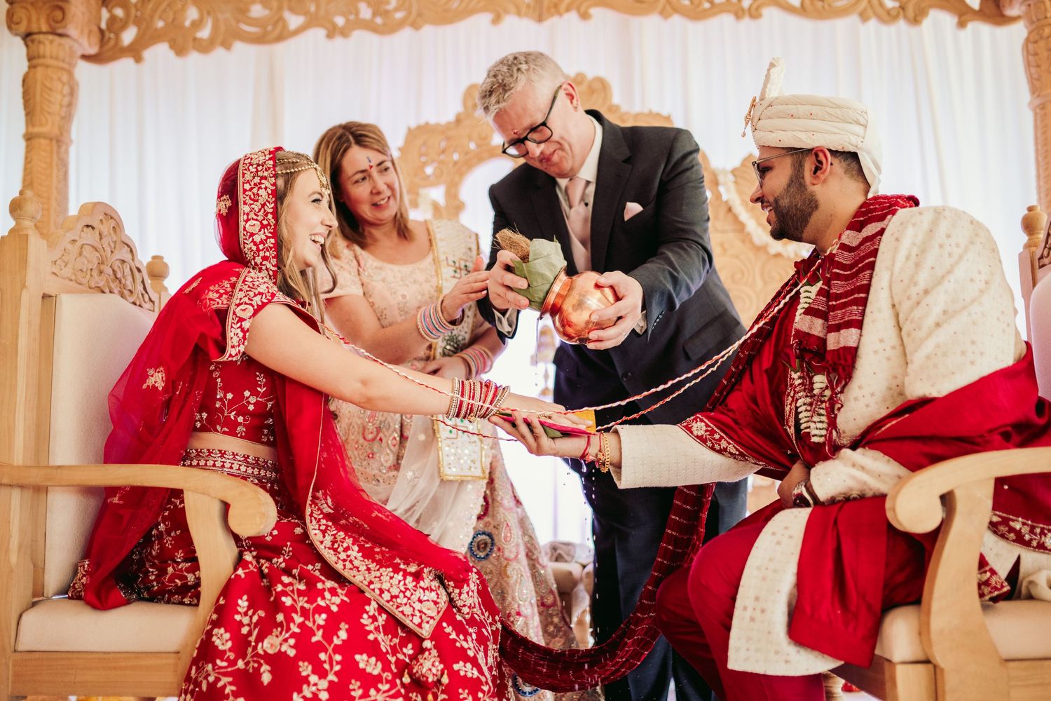 Traditional Indian wedding ceremony showing participants performing rituals with vibrant red and gold attire decorations.