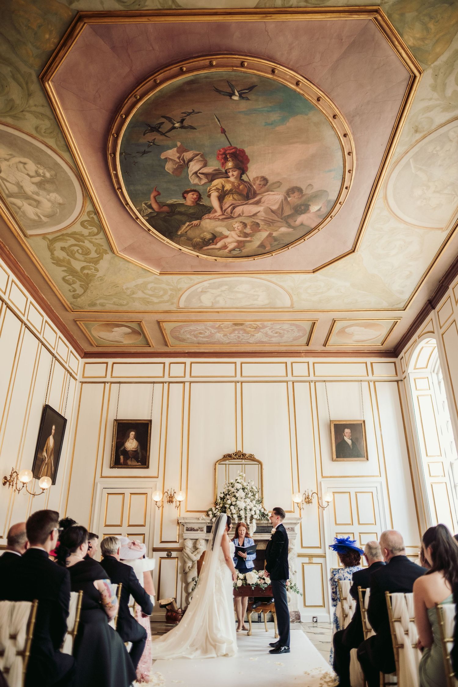 Wedding ceremony in grand ballroom with ornate ceiling fresco and classical architecture.