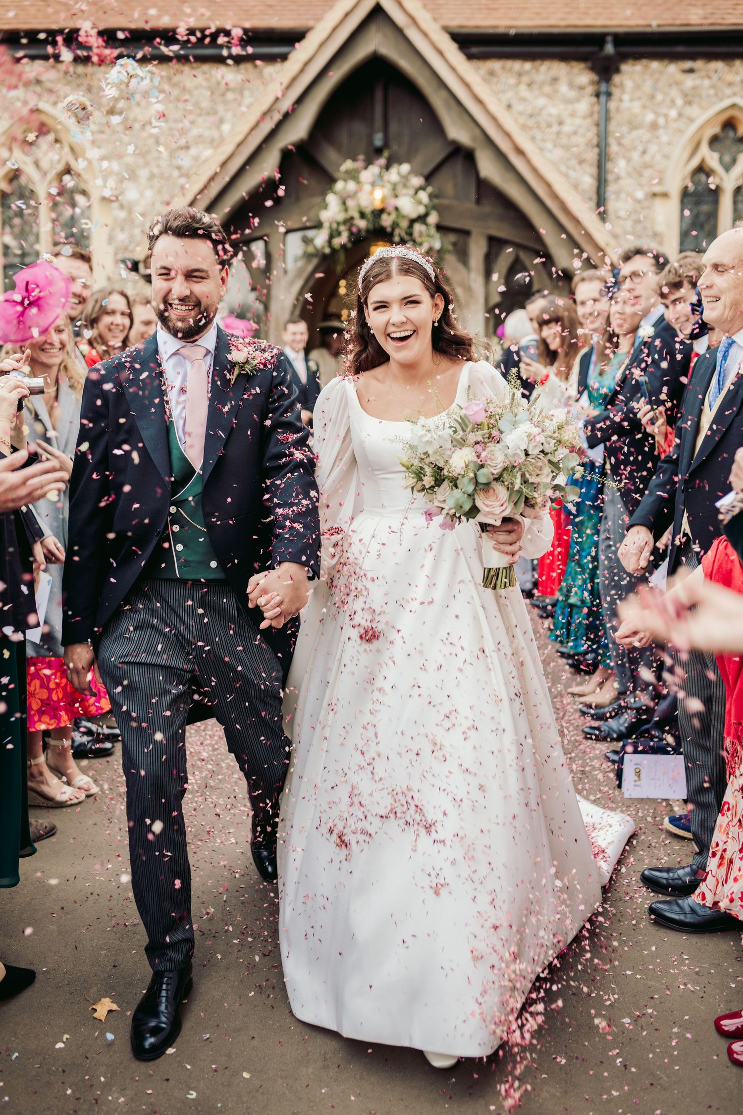 Wedding exit with pink confetti shower outside stone church entrance.