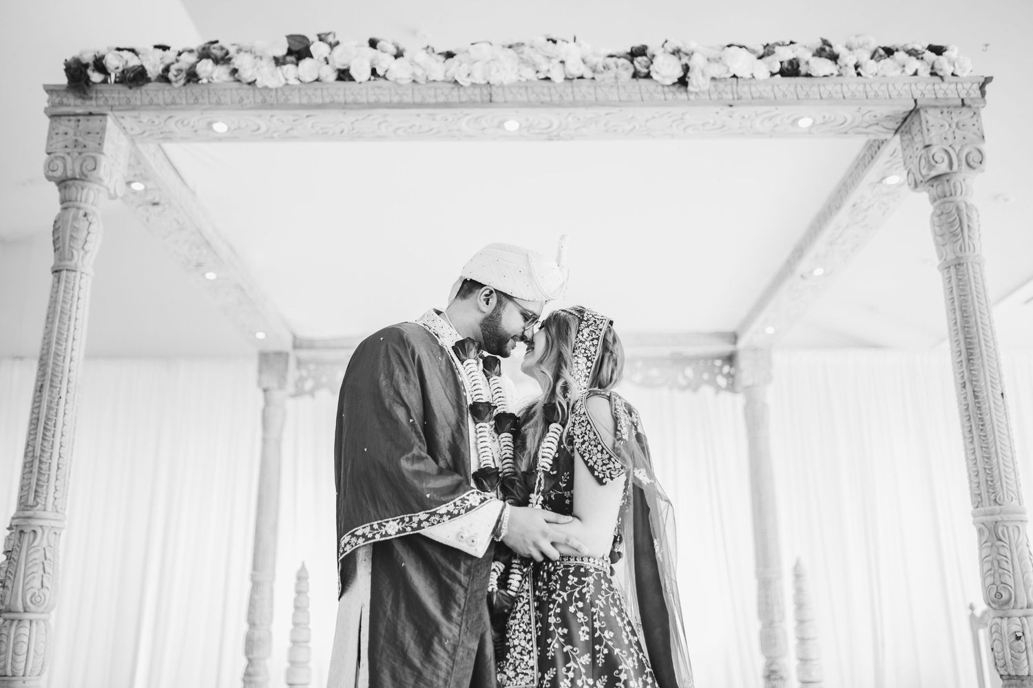 Black and white romantic moment captured under an ornate decorative archway during a traditional cultural celebration.
