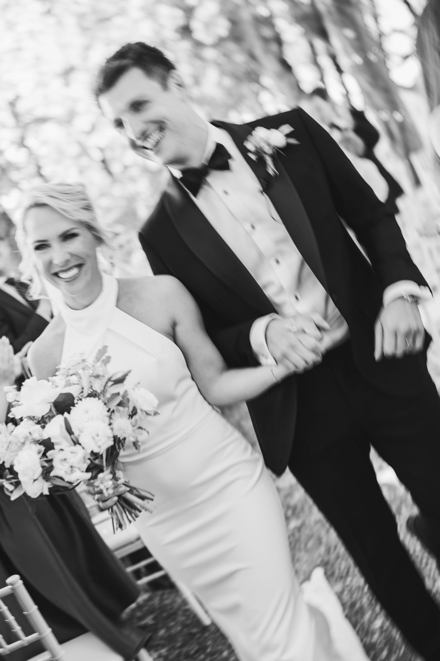 Black and white wedding photo of couple walking outdoors with bridal bouquet.