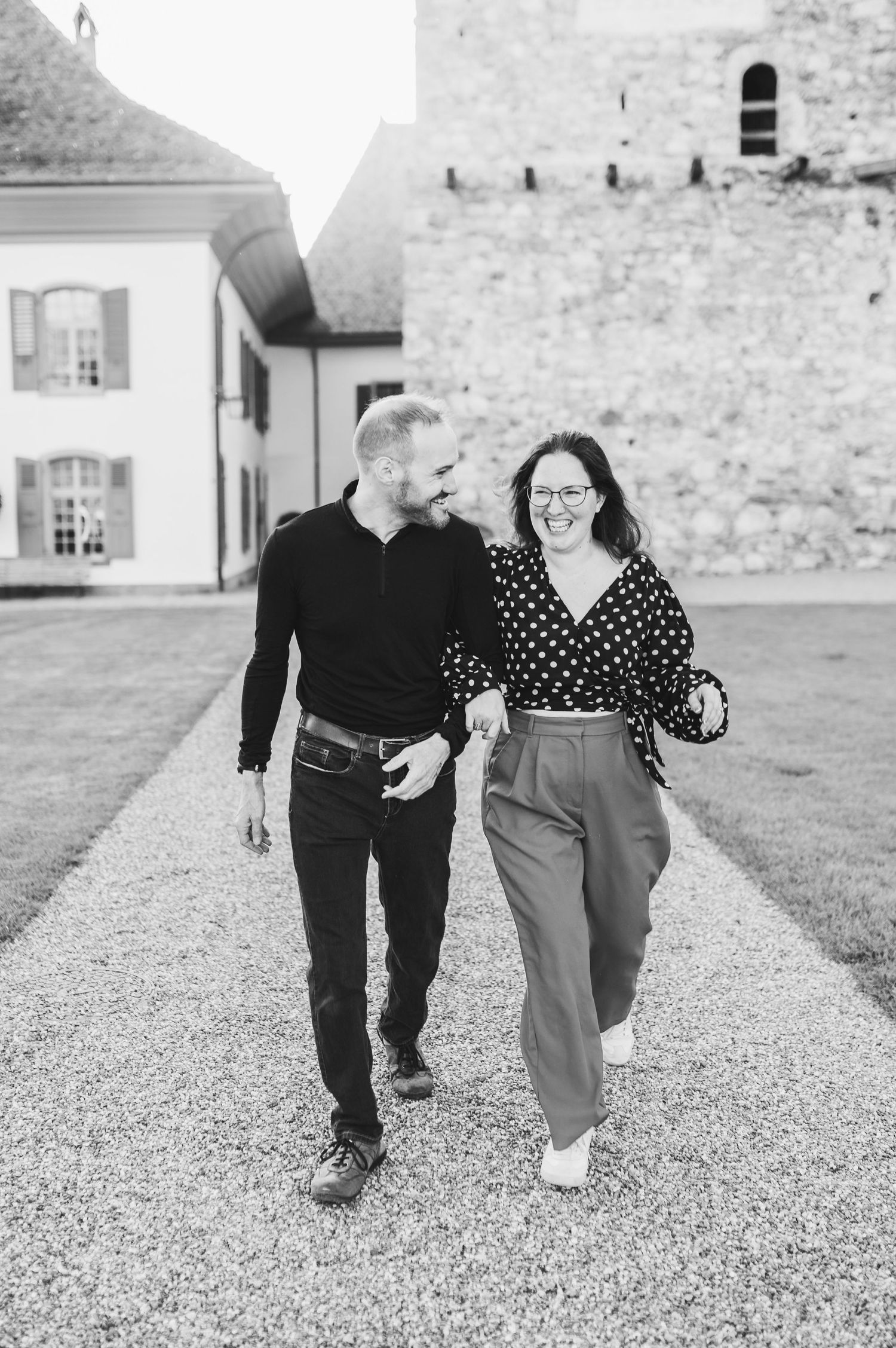A couple walks together on a gravel path outside a historic building in black and white photography.Spiez switzerland destination wedding
