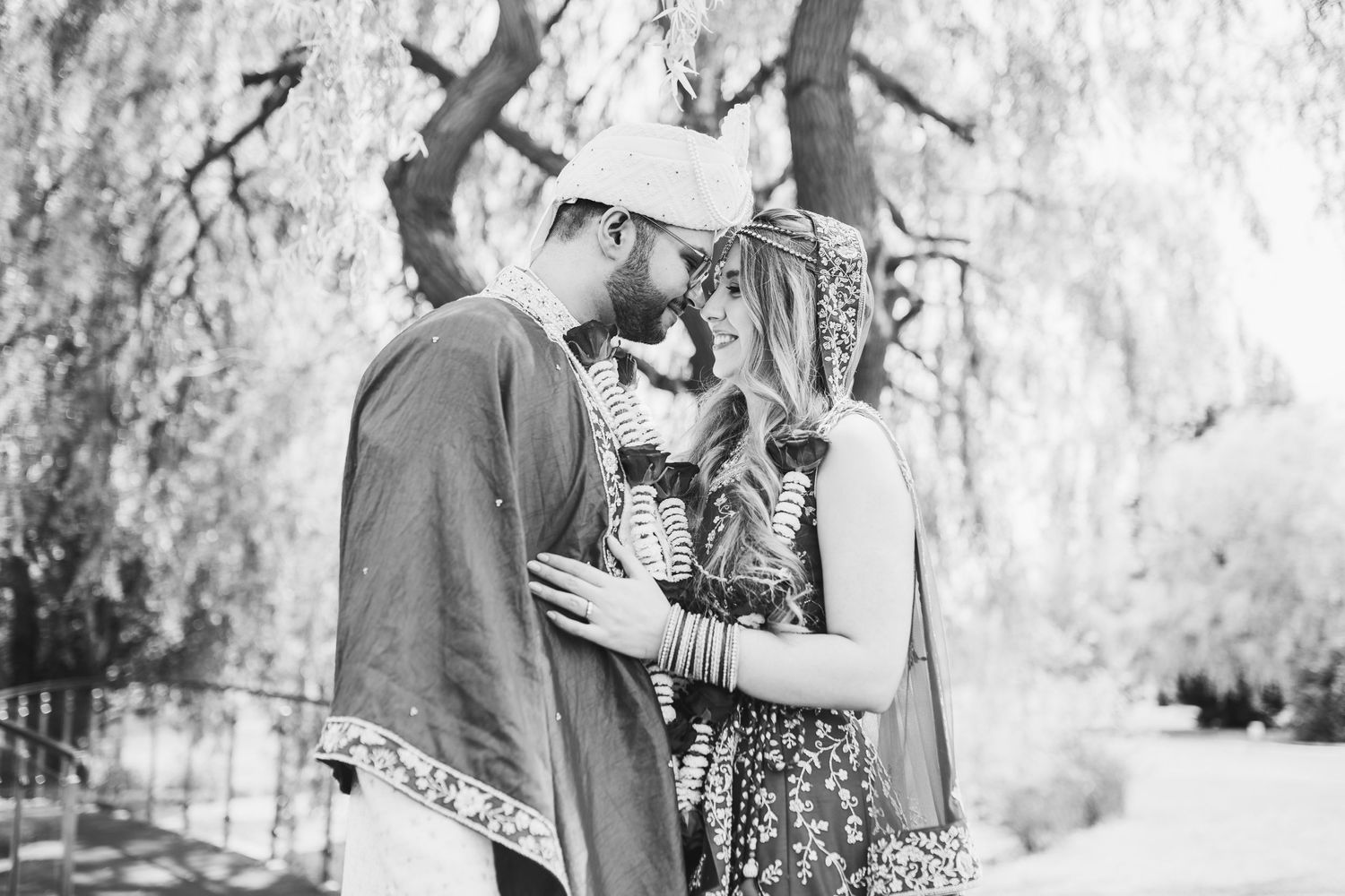 A romantic black and white photo of a couple in vintage clothing embracing outdoors beneath a tree.