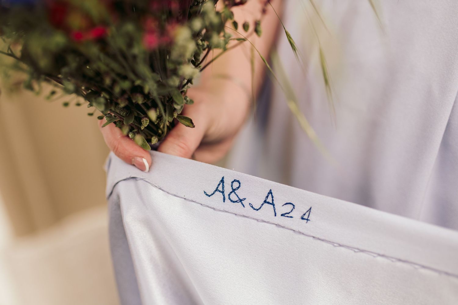 A hand holds white fabric with embroidered text 