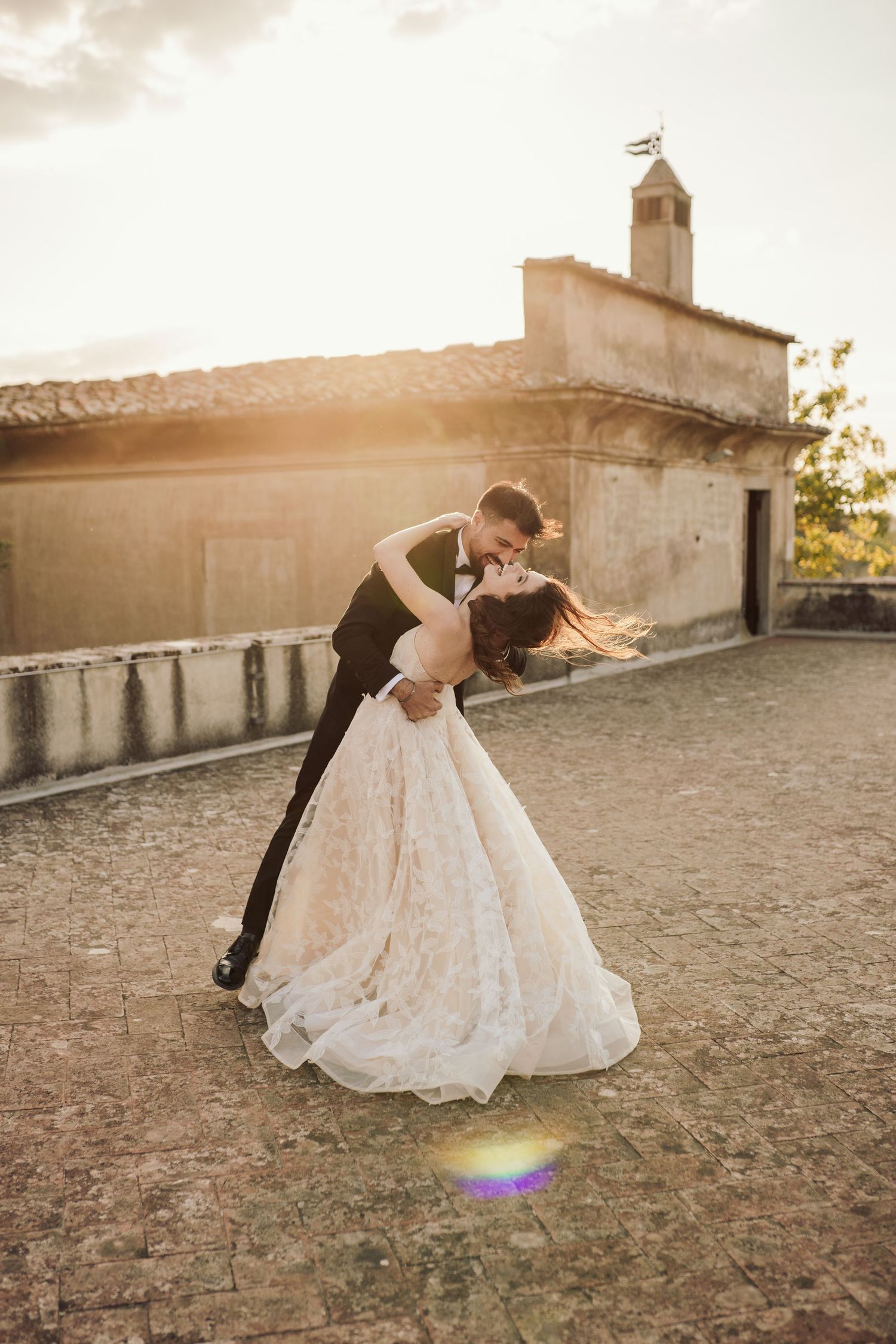 Romantic sunset wedding portrait with couple dancing in front of Mediterranean building.