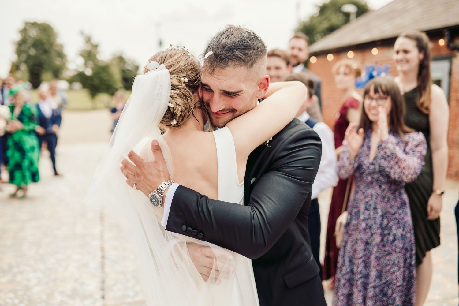 Joyful wedding celebration with couple embracing while guests look on at outdoor venue.
