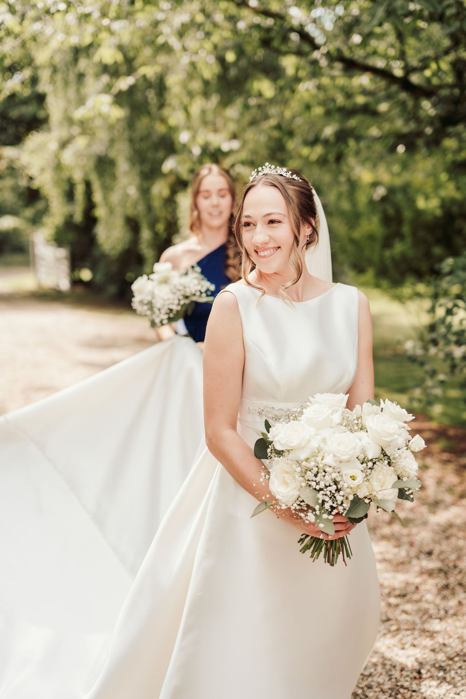 A bride in a classic white wedding dress holds a beautiful bouquet of white flowers in an outdoor garden setting.