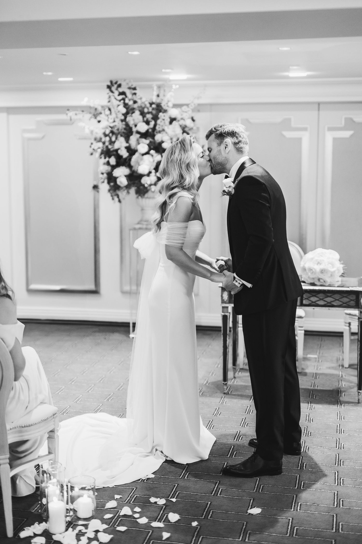 A couple shares an intimate moment during their wedding ceremony with elegant floral arrangements in the background.Claridge’s wedding