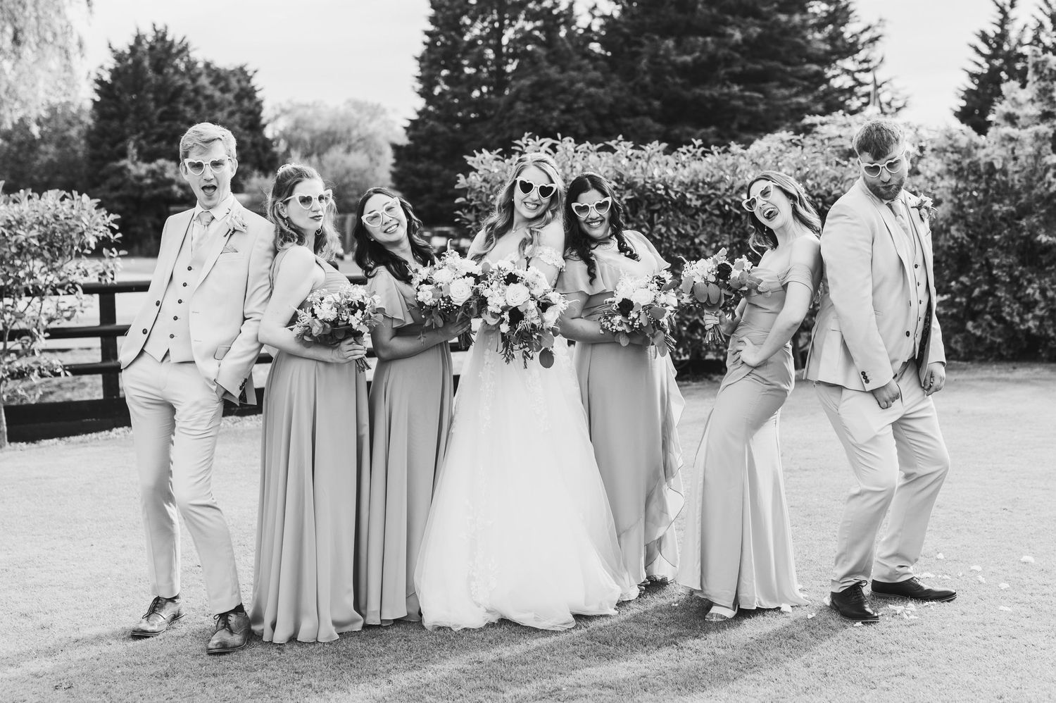 Black and white wedding photo showing a bridal party laughing together outdoors with bridesmaids in flowing dresses.
