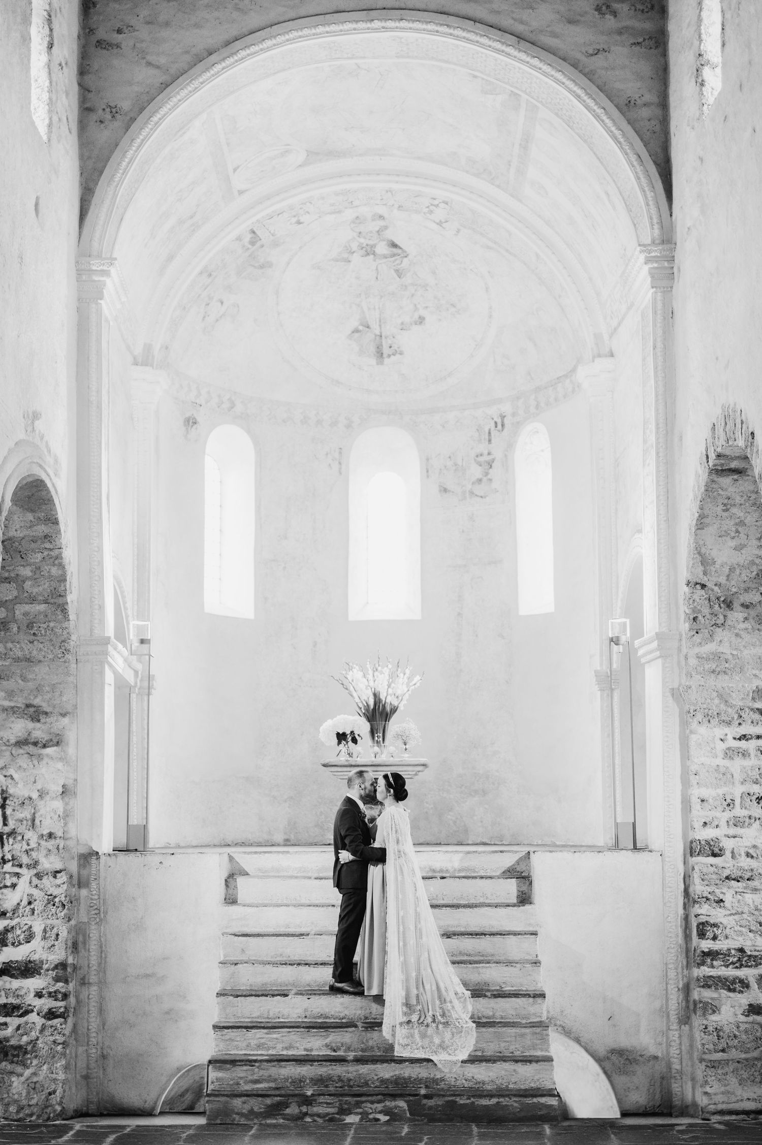 A couple stands intimately at the altar of a bright white stone church with arched windows and vaulted ceiling.Spiez switzerland destination