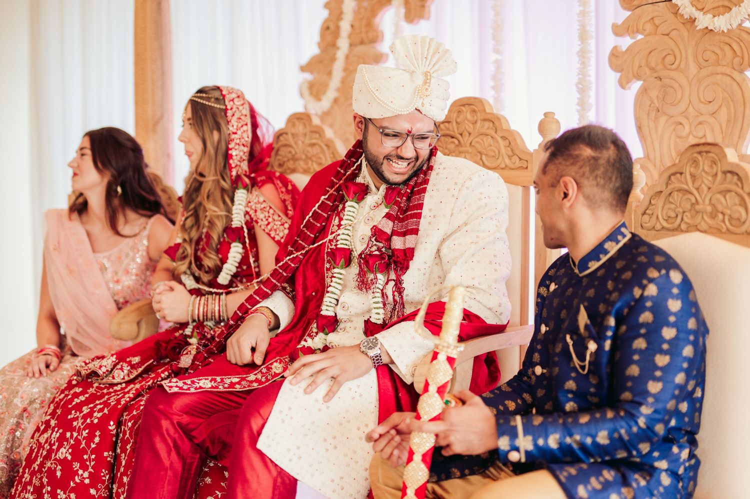 Wedding ceremony guests in traditional South Asian attire seated on ornate throne with elegant decor at cultural celebration.