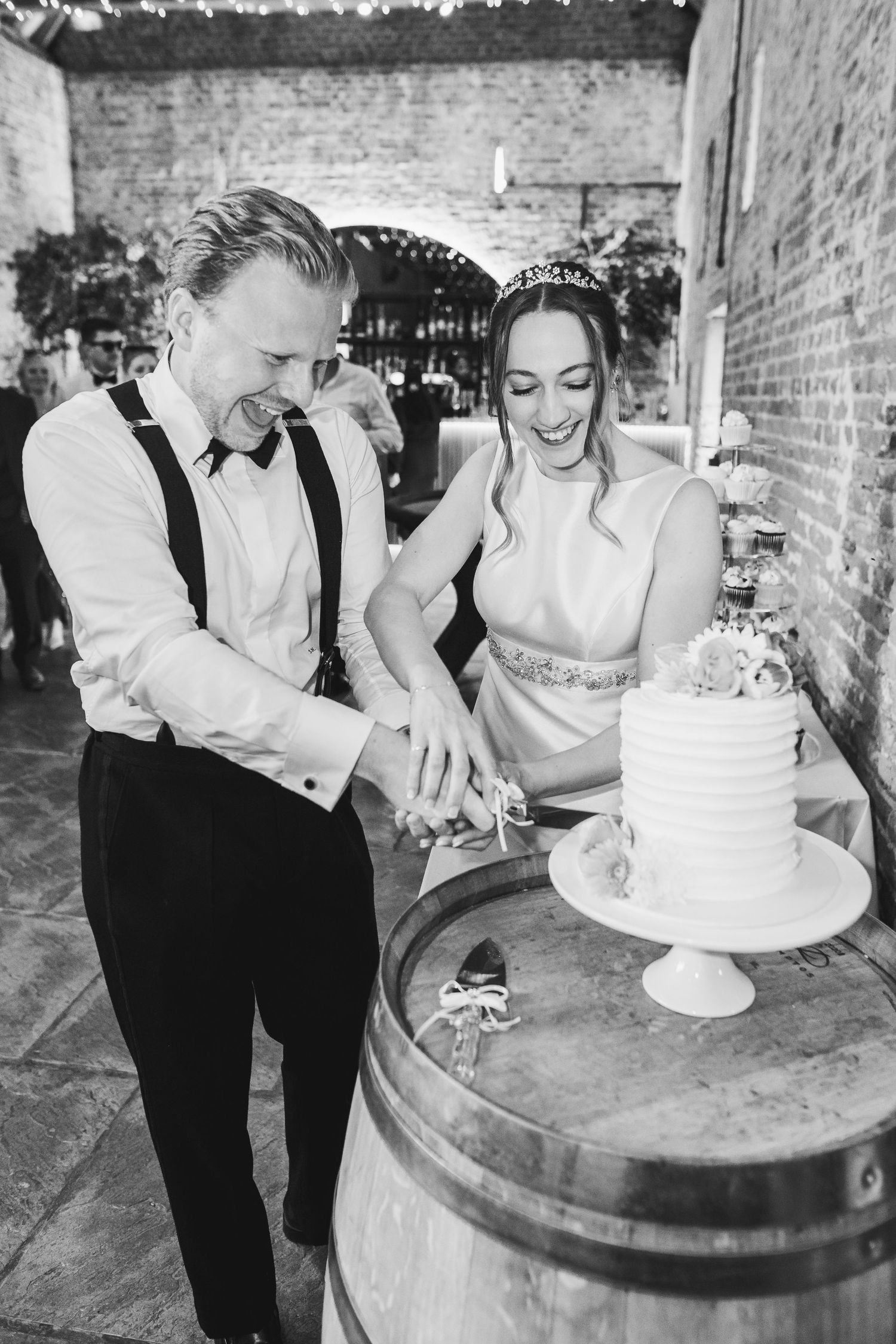 A black and white photo series of a couple cutting their wedding cake together on a rustic wine barrel.