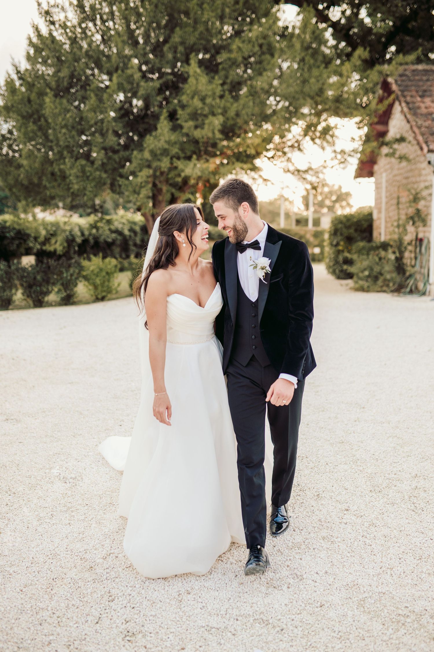 A couple in formal wedding attire walking and posing together on a gravel path.